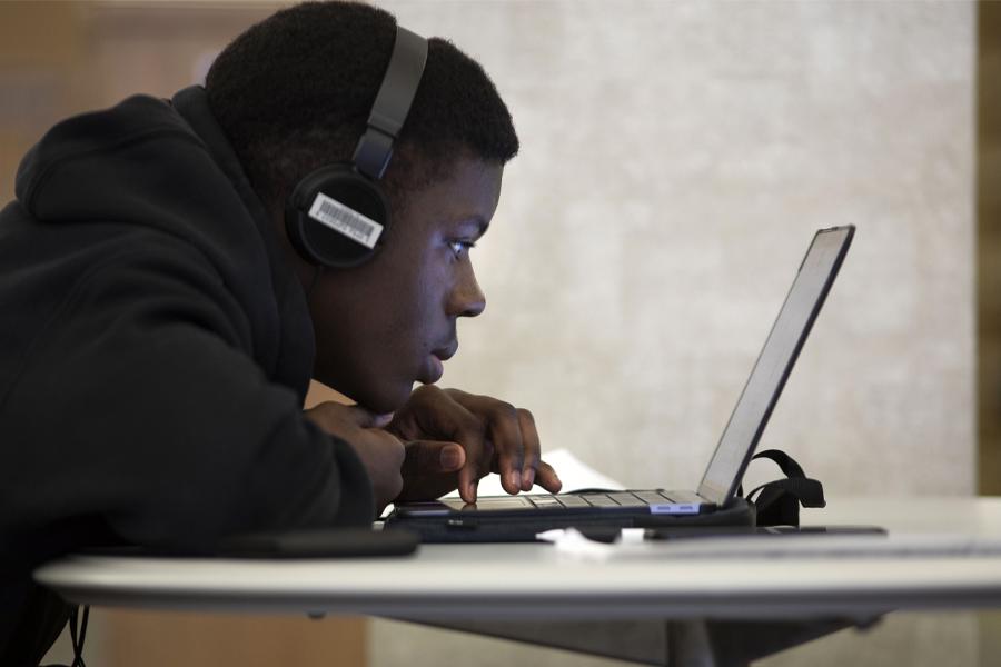 A student works on a laptop while wearing headphones.