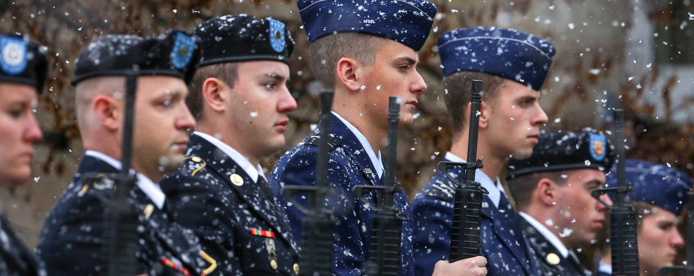 Veterans stand with their rifles as it snows.