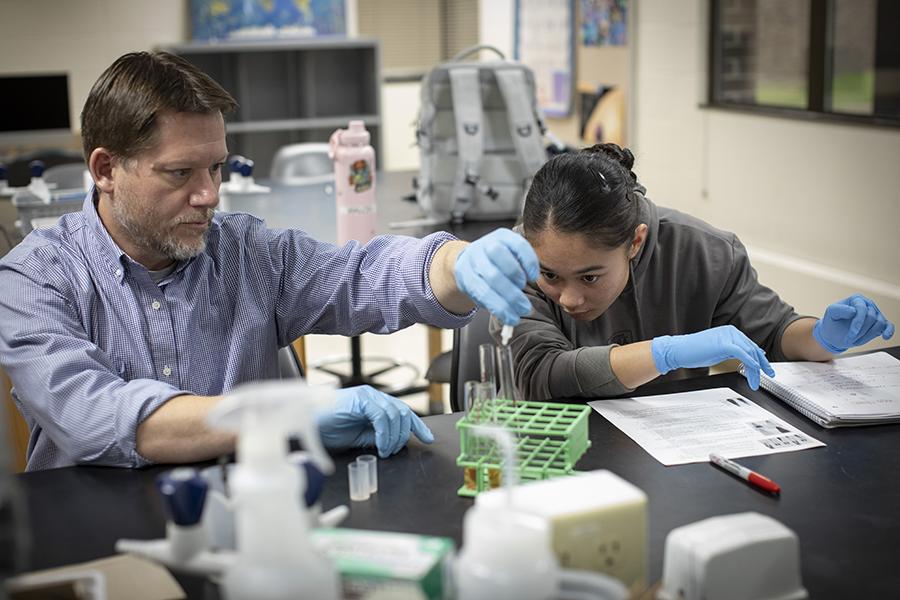 A student and faculty member work in a lab with vials and test tubes.